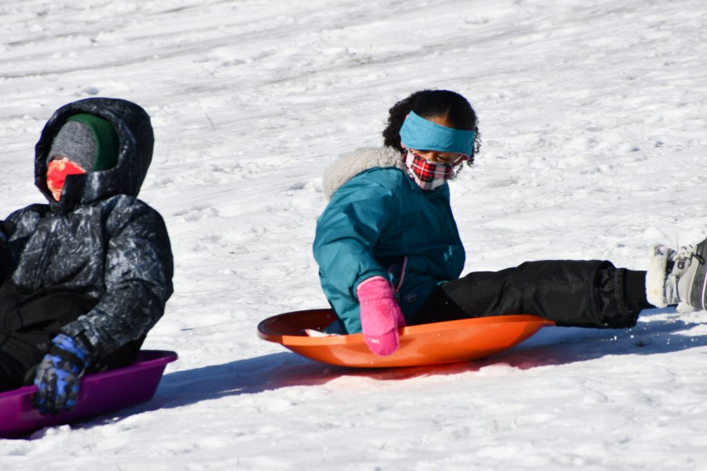 Students on sleds slide down a snowy hill.