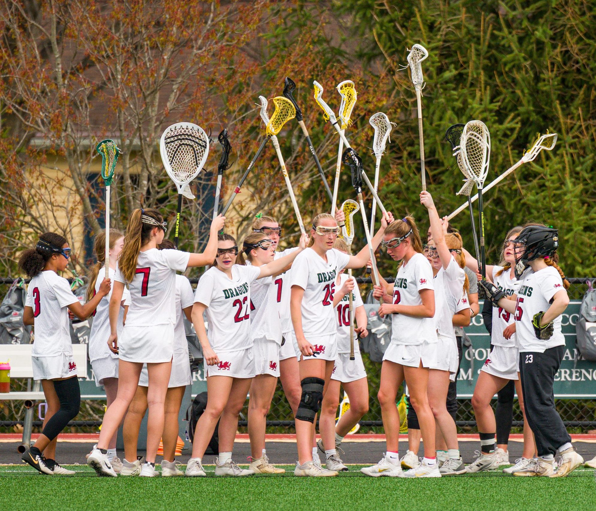 Group of female student athletes wearing white lacrosse uniforms. The girls have lacrosse sticks in their hands.