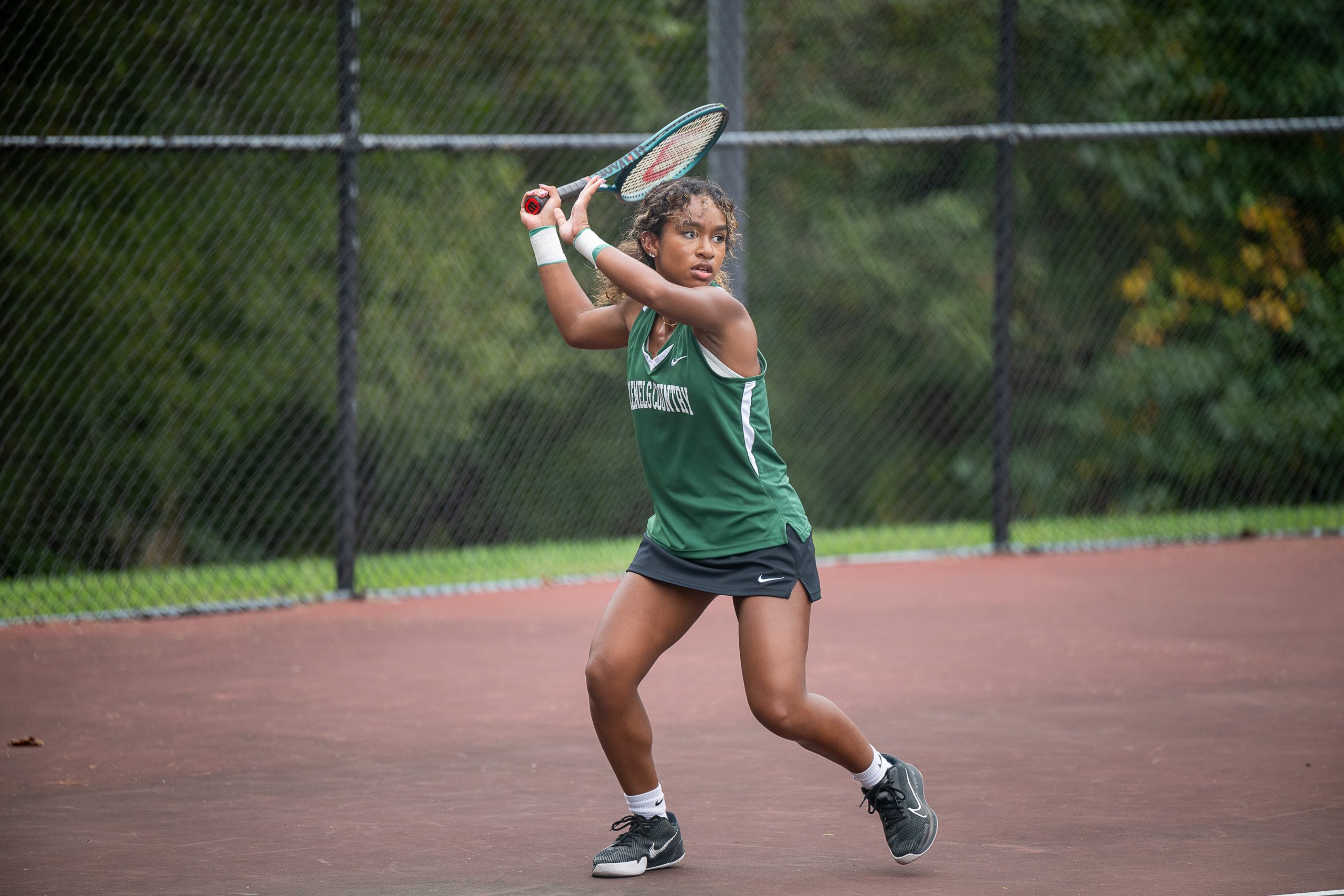 A female student athlete, wearing green tennis uniform plays tennis on tennis court.