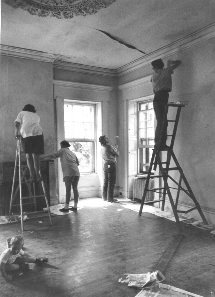 Two people on a ladder and two people standing, all painting walls.