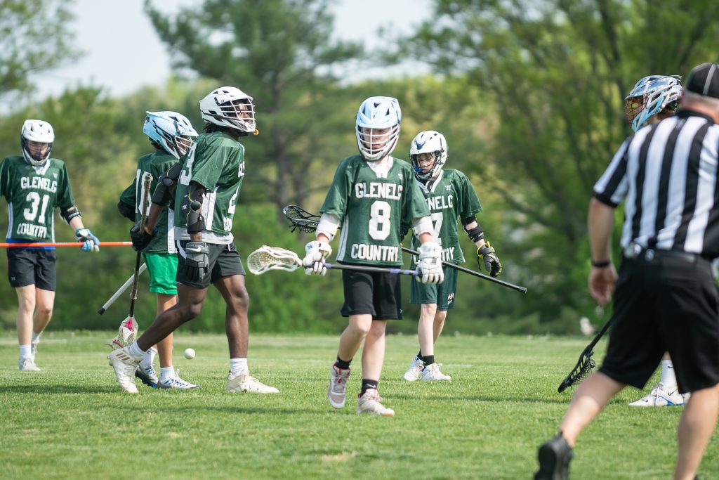 Five male student athletes playing lacrosse in green uniforms.