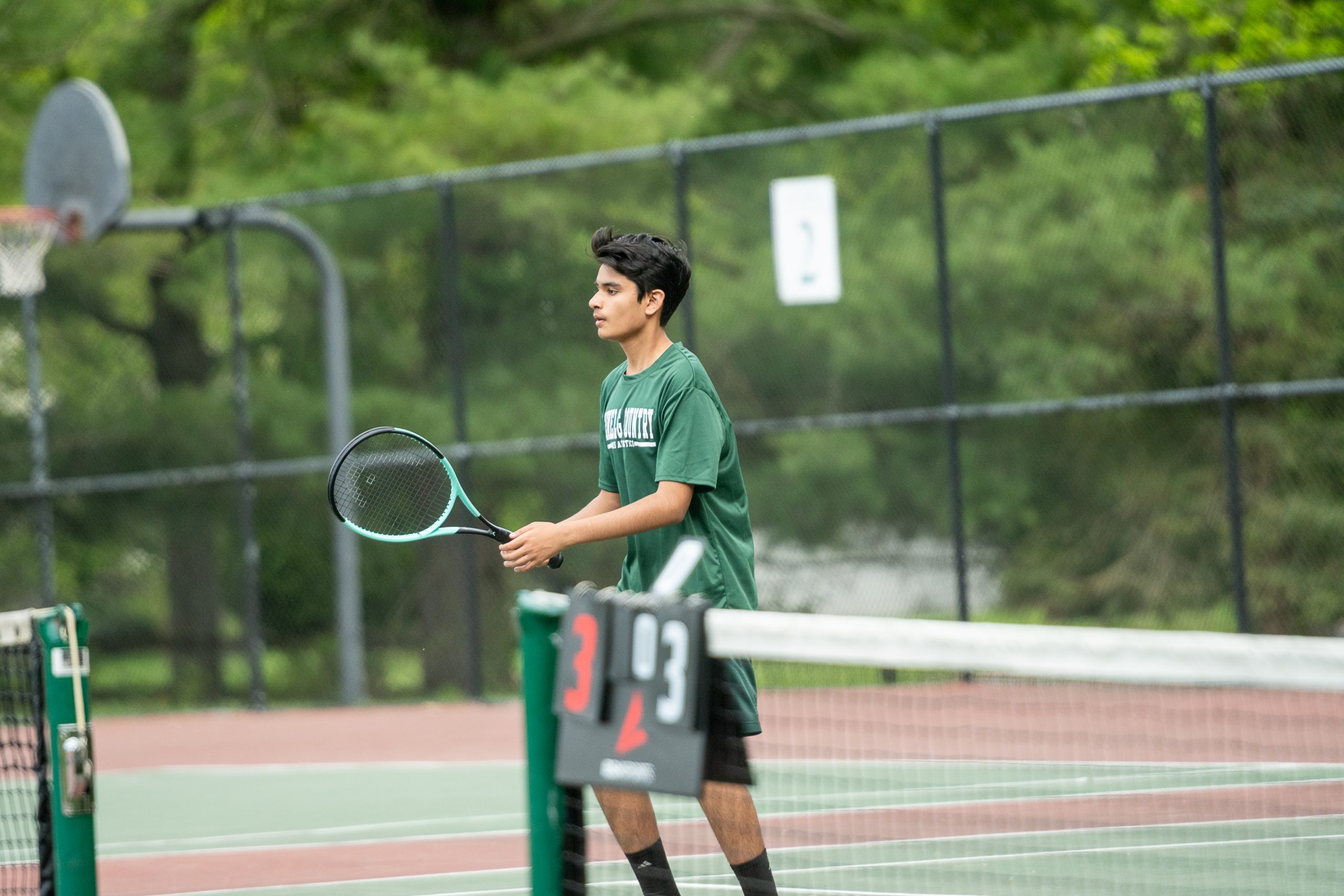 Male student athlete playing tennis in a green uniform.