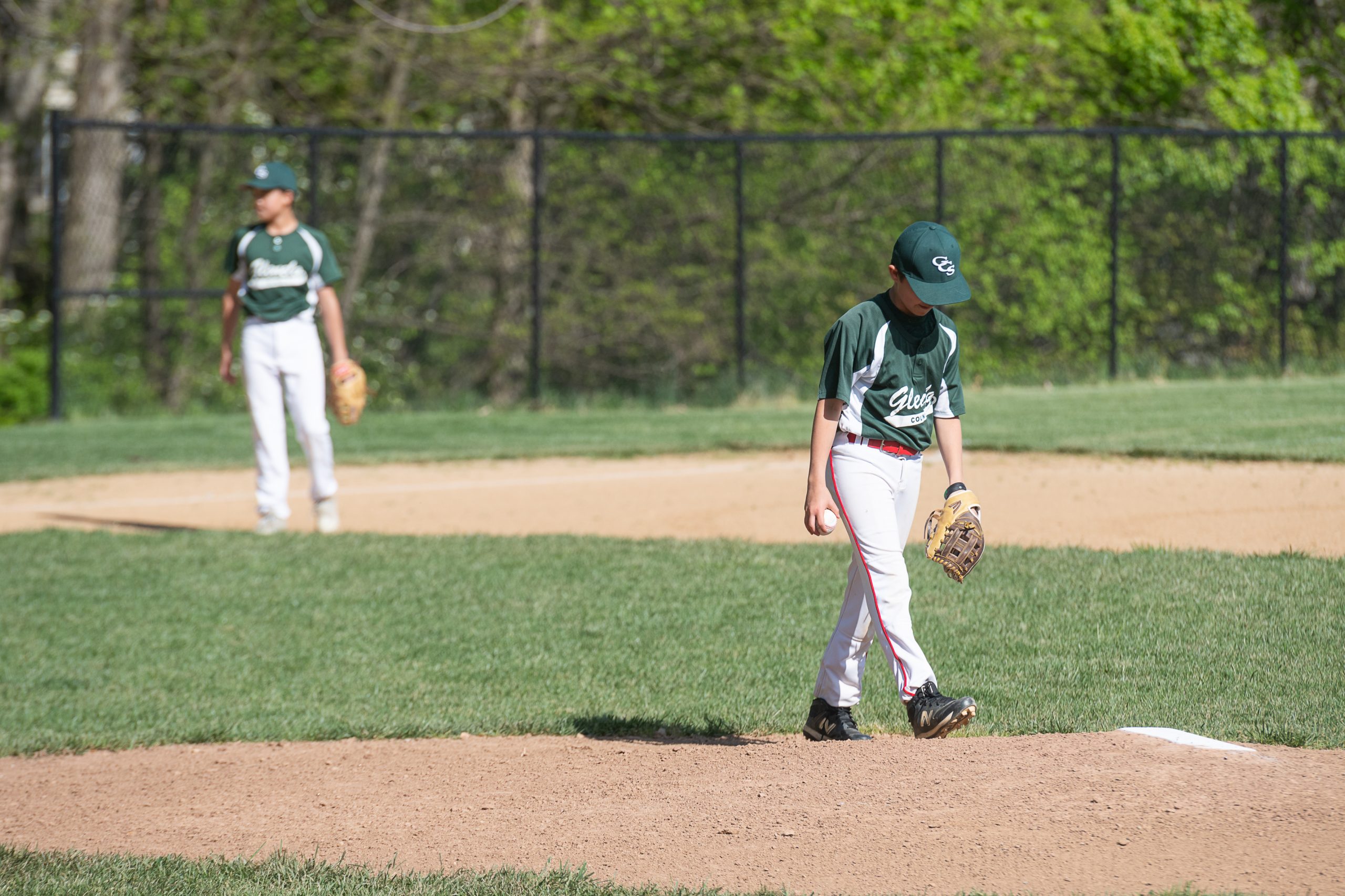 Two male student athletes playing baseball. Both are wearing green jersey tops and white pants.