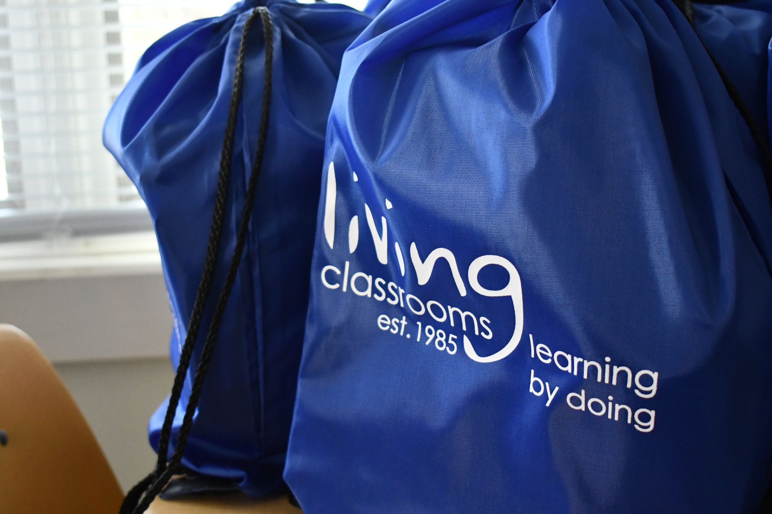 A blue backpack with the Living Classrooms logo sits on a desk.