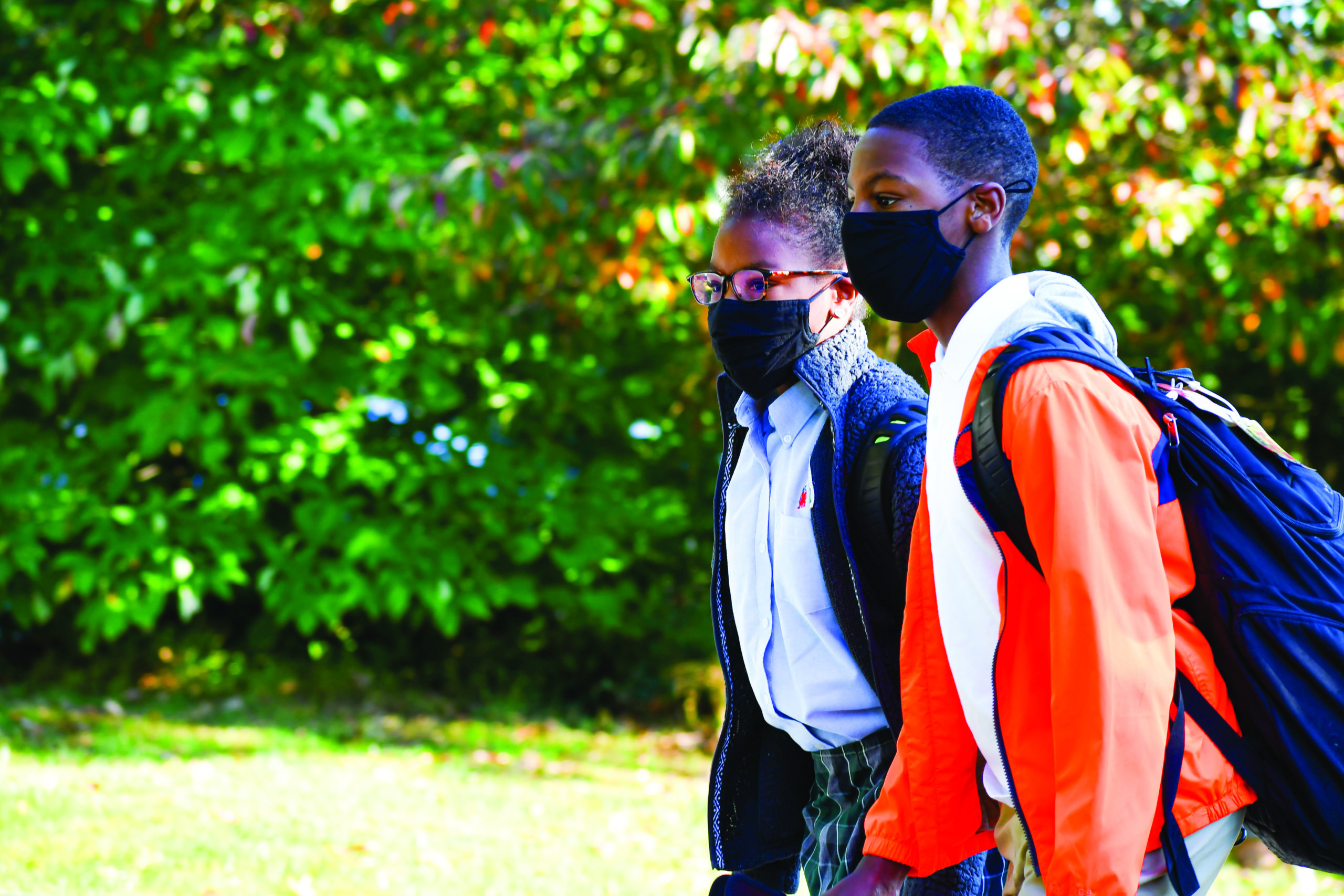 A boy and girl wearing masks walk outside.
