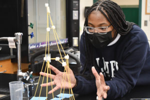 A Biology student looks at her spaghetti and marshmallow tower.