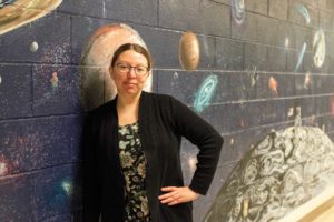 Krystal Rolon leans on a wall mural depicting the solar system.