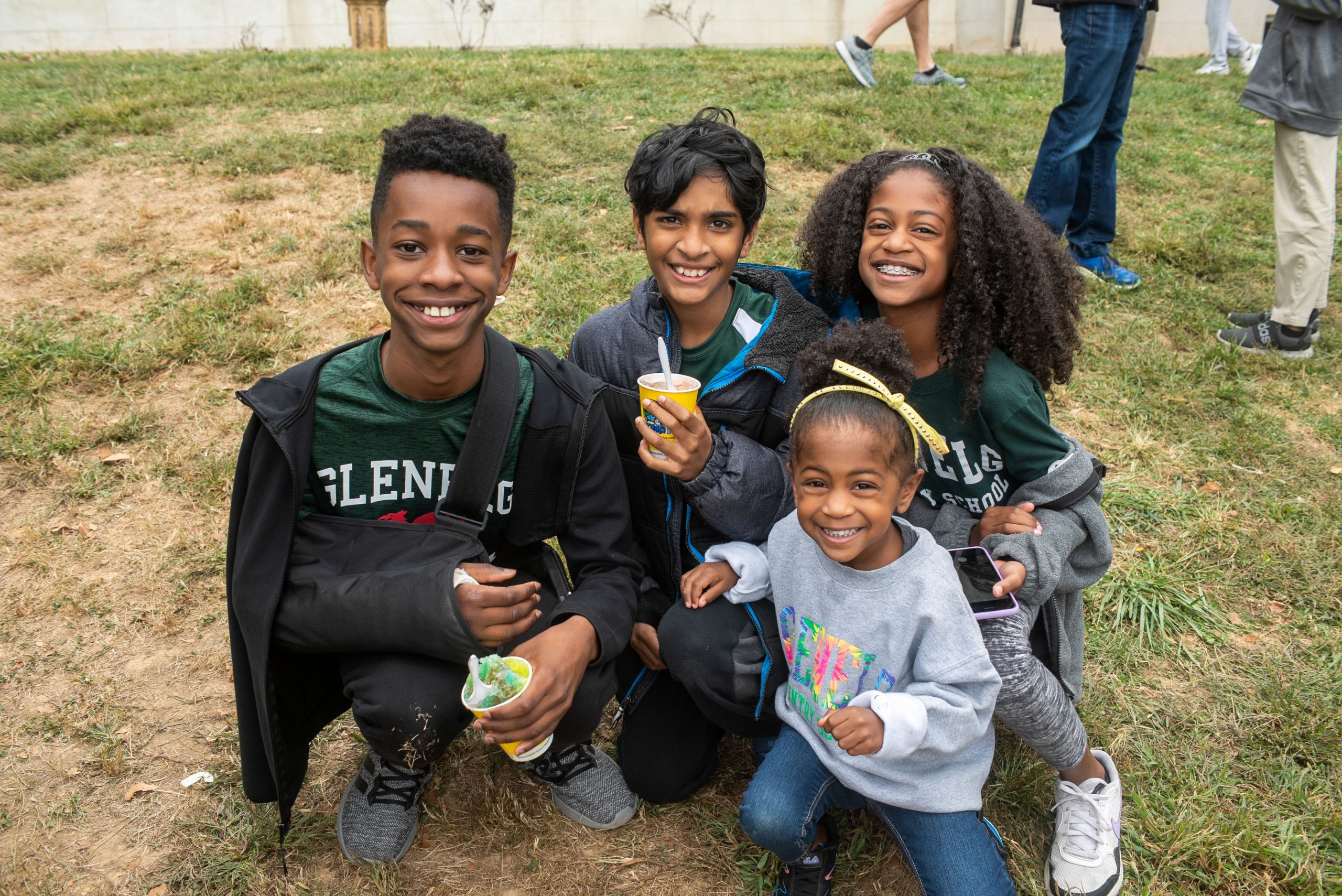 Four students smile at the camera as they sit on the ground enjoying snowballs during Family Day 2022.