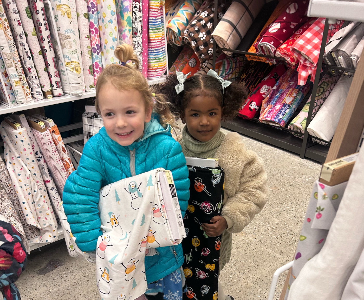 Two three-year-old girls hold fabric rolls inside of the Joann Fabrics during a recent field trip.