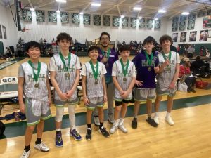 Middle school-age boys in basketball uniforms lined up and smiling with winning medals.