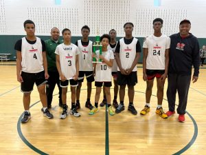 A youth boys basketball team poses at center court with their coach and a championship trophy.