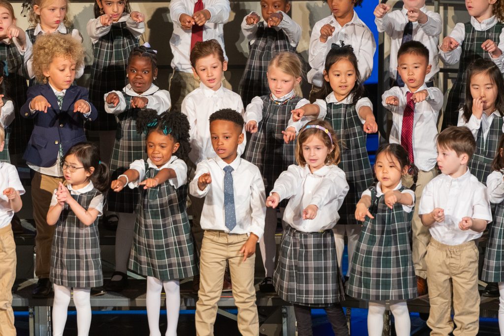 first grade students in uniform point at the audience during a performance.