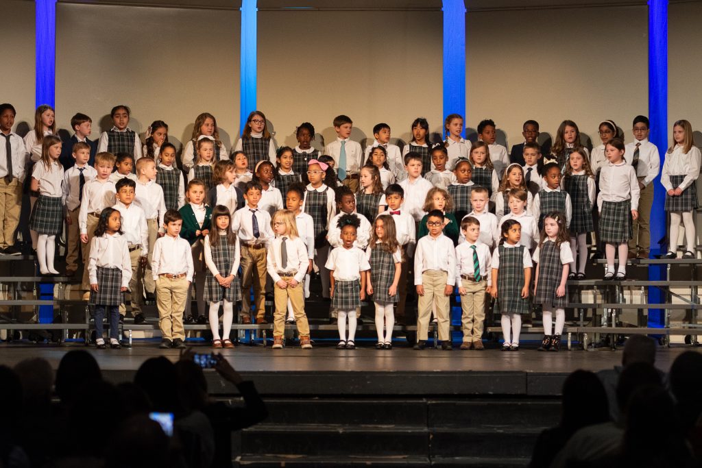 A large group of school children perform onstage.