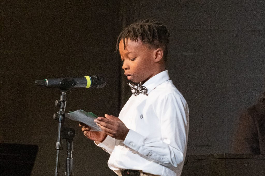 young student in bowtie speaks into a microphone.