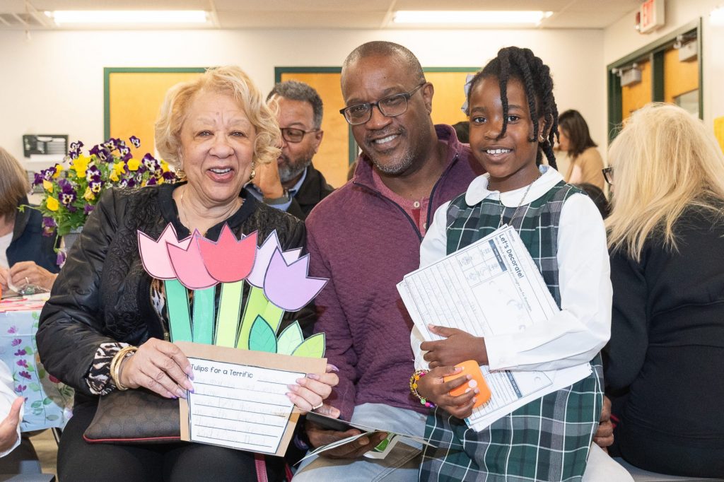 Grandparents pose with their granddaughter and a craft project.