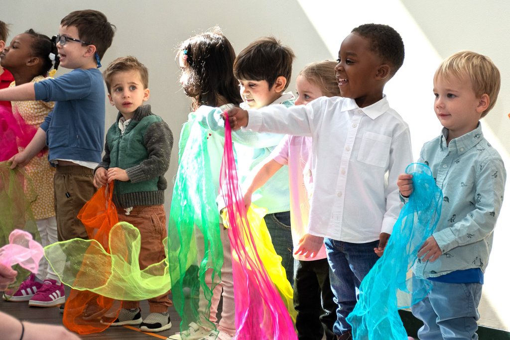 Preschool children wave colorful scarves during performance.